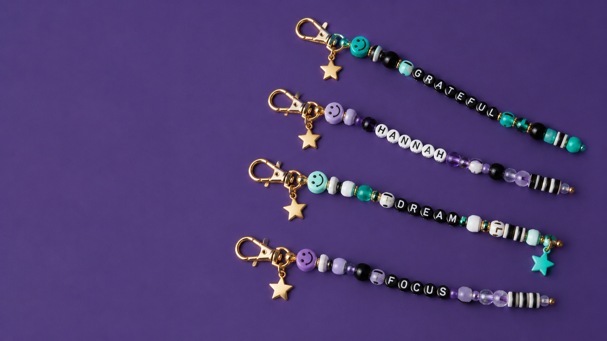 Four personalized beaded keychains with names and words on a purple background.
