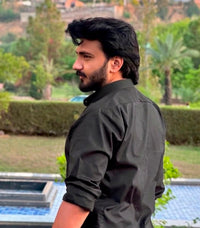 Side profile of a bearded man in a black button-down shirt outdoors.