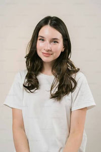 Smiling young woman with long wavy brown hair wearing a white t-shirt.