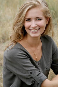 Smiling young woman with blonde hair wearing a grey button-down shirt outdoors.